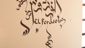 Een muur met Arabische kalligrafie en een lijst met een schilderij van twee figuren.