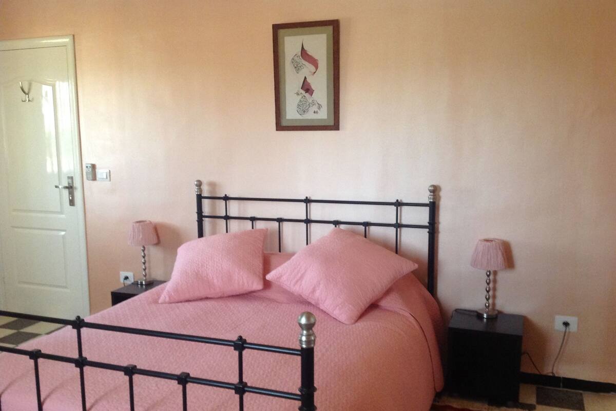 A bedroom with a bed, two bedside tables, a door, and a framed picture on the wall.