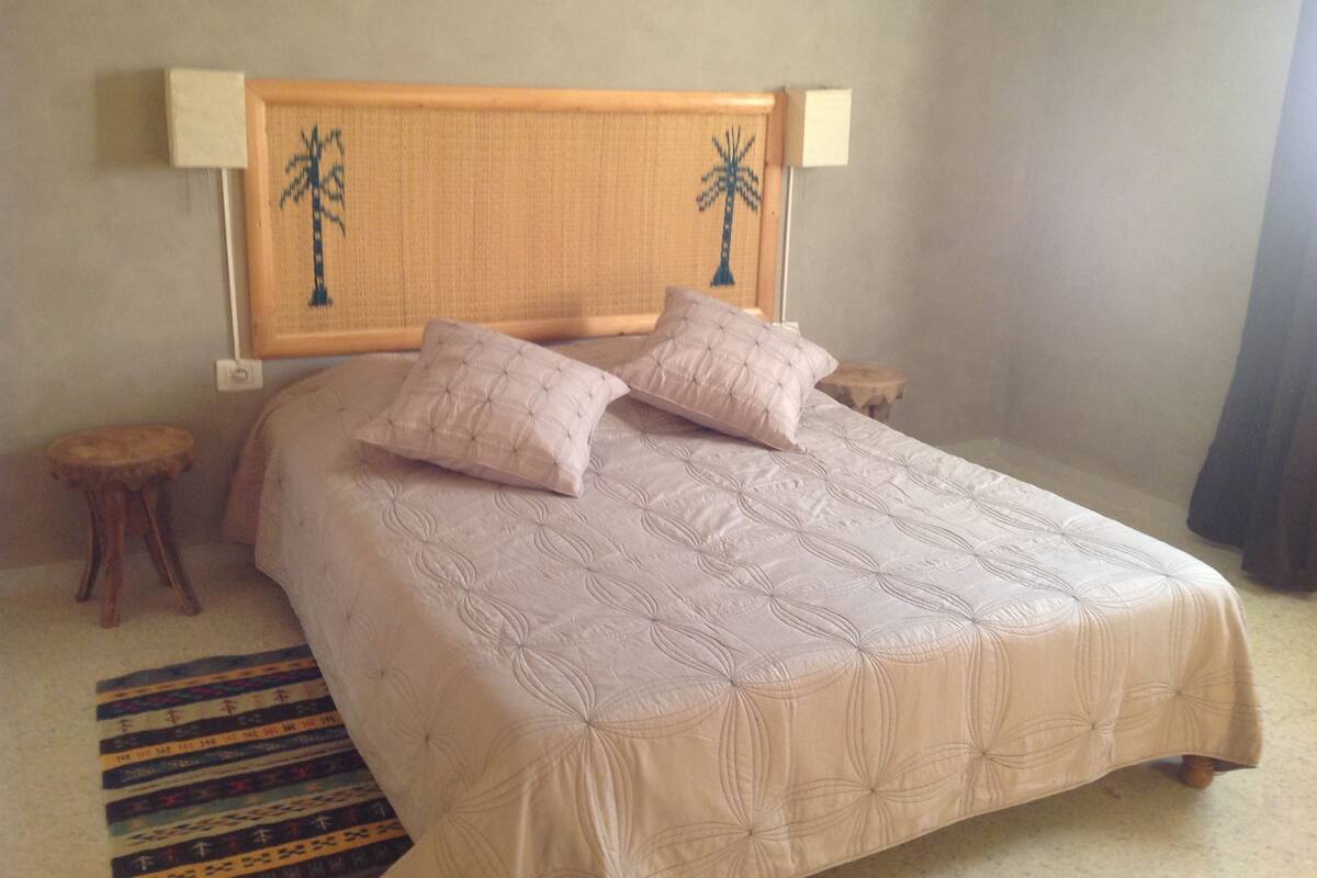 A bed with a headboard featuring palm tree designs, two pillows, and a striped rug.