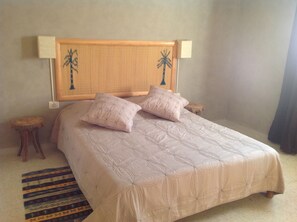 Una cama con cabecera decorada con motivos de palmeras, dos almohadas y una alfombra a rayas.