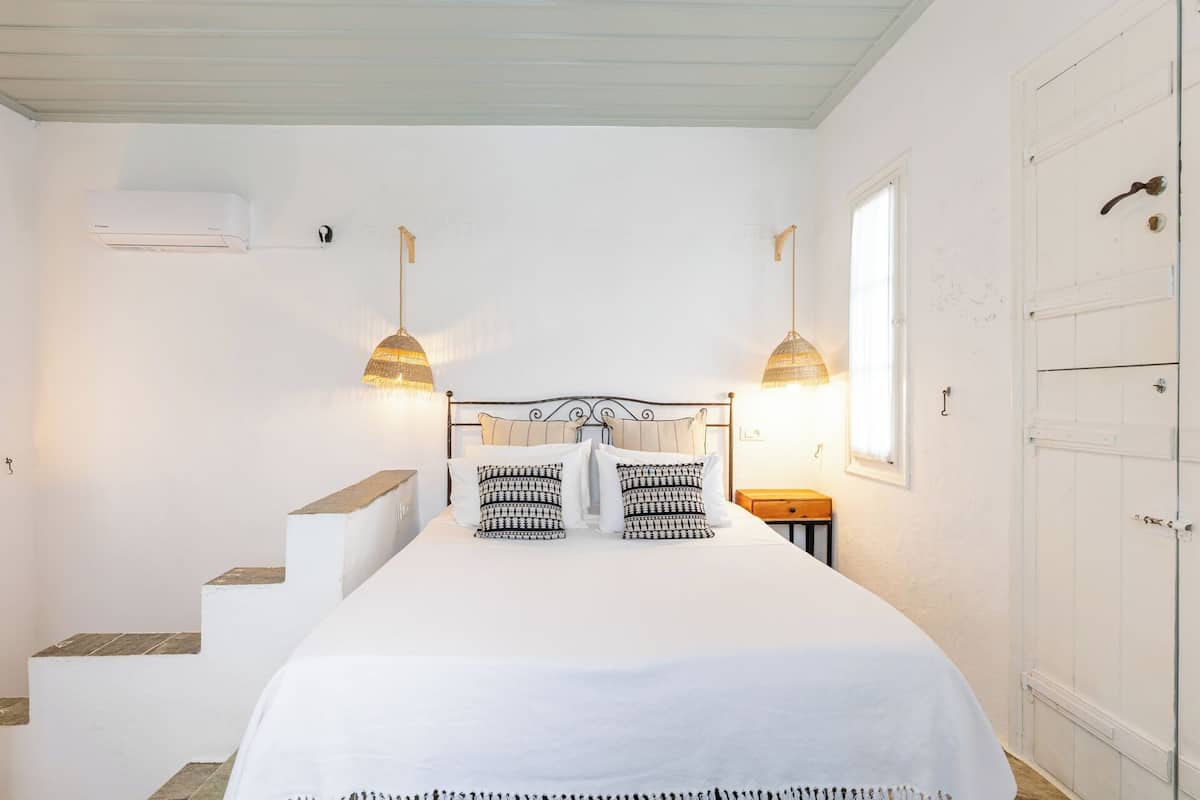 A bedroom with a bed, two hanging lamps, a window, and a door.