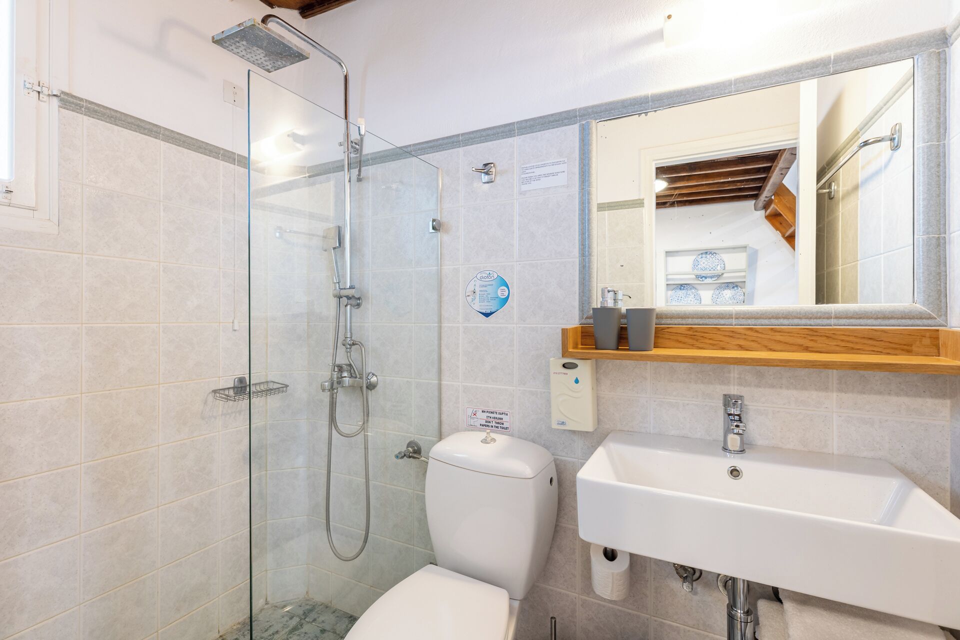 A modern bathroom with a glass-enclosed shower, a toilet, and a sink with a wooden shelf above.
