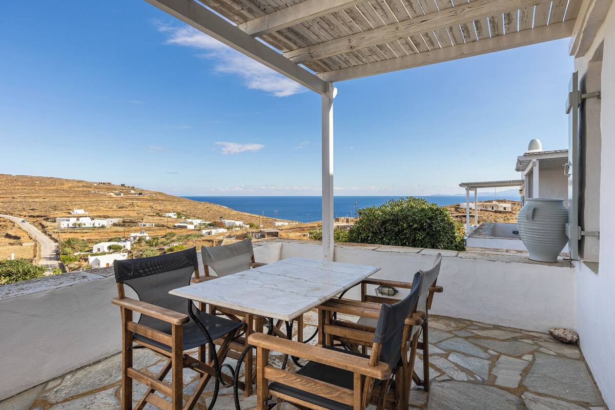 A terrace with a table and chairs, overlooking a coastal landscape with buildings and the sea.