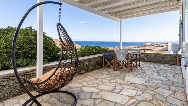 Un espace extérieur aménagé, abrité et doté de sièges, avec un fauteuil suspendu, un sol en pierre et une vue sur la mer.