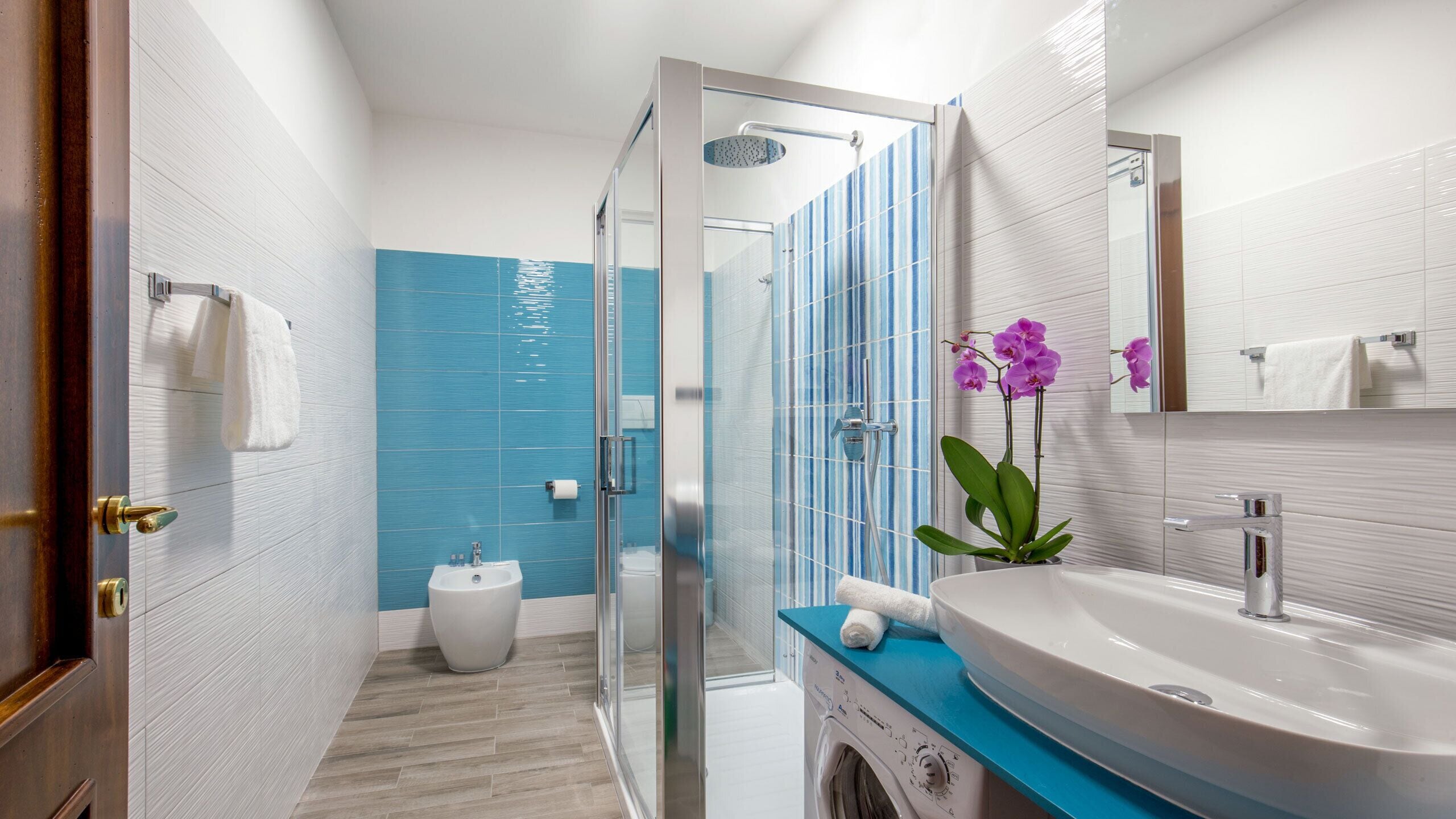 Un baño moderno con cabina de ducha de vidrio, un lavabo con encimera azul y un espejo sobre el lavabo.