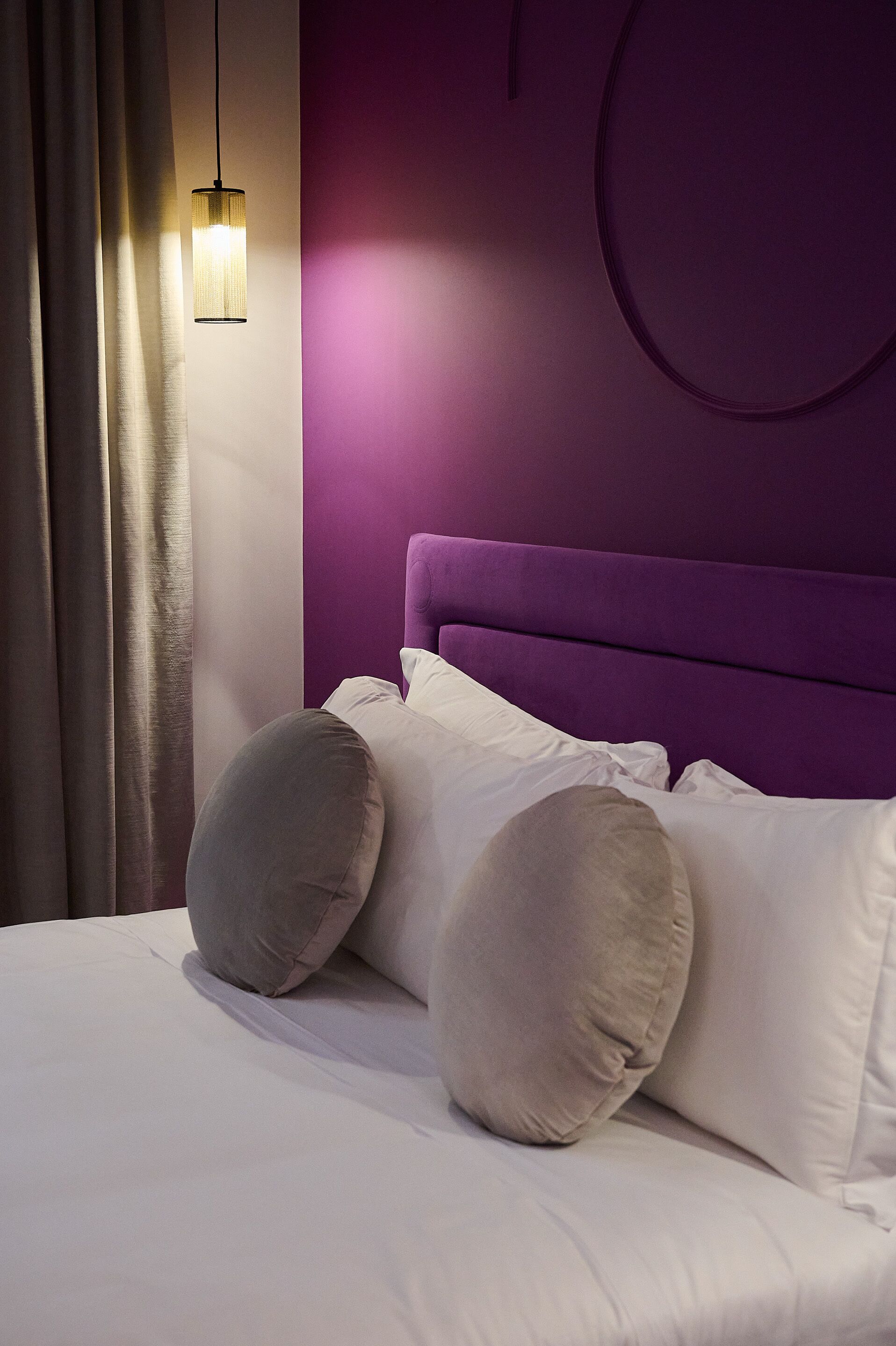 A bedroom with a purple headboard, white bedding, and a hanging light fixture.