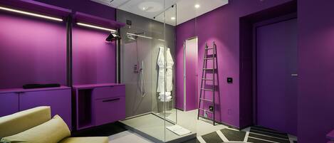 Une salle de bain moderne avec des murs violets, une douche en verre, un canapé jaune et un sol à motifs géométriques.