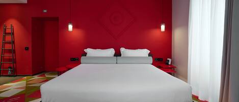 A modern hotel room with a large bed, red walls, and a geometric patterned carpet.