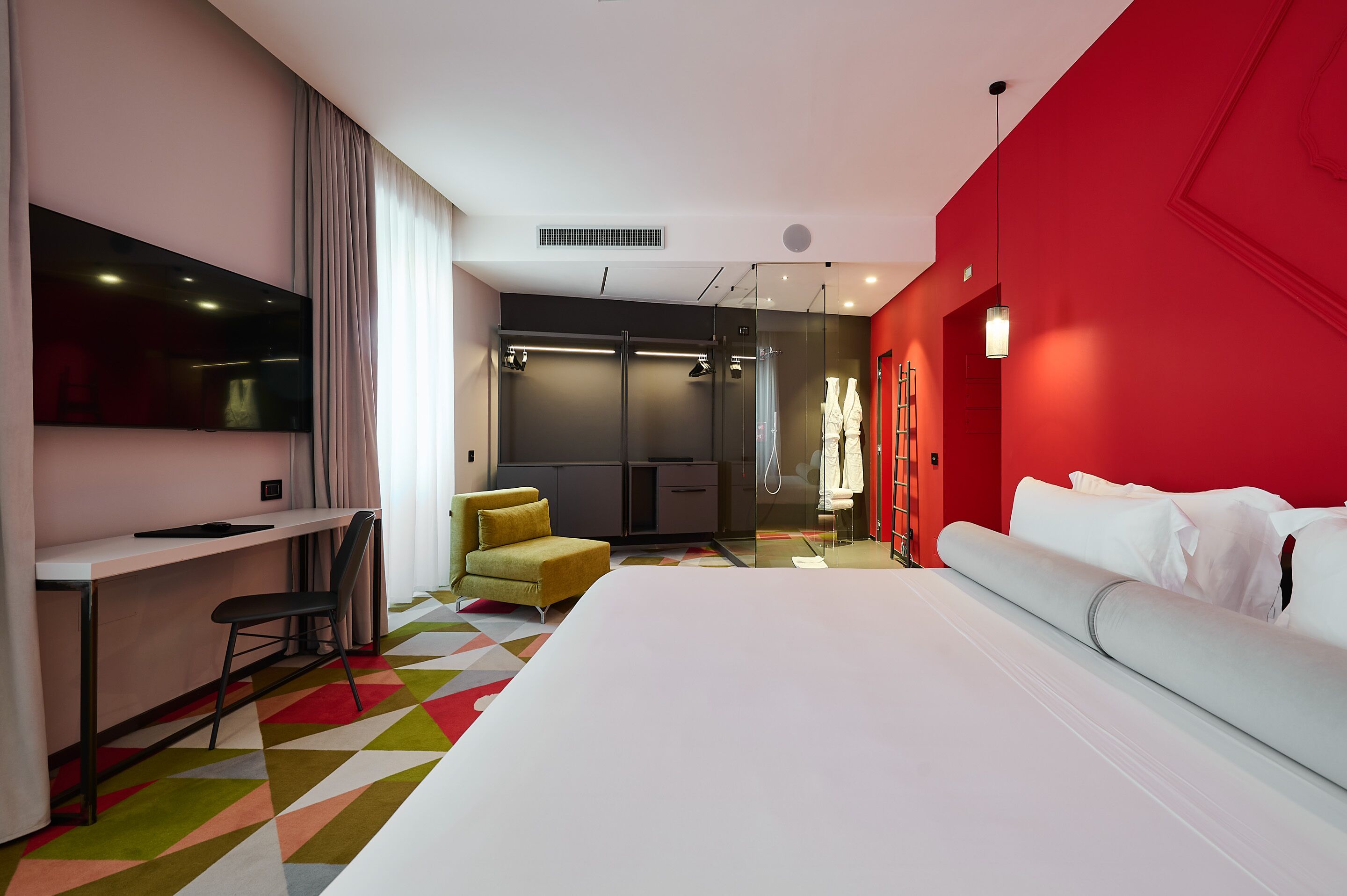 Ein modernes Hotelzimmer mit einem großen Bett, einem Schreibtisch, einem Sessel und einer Duschkabine.