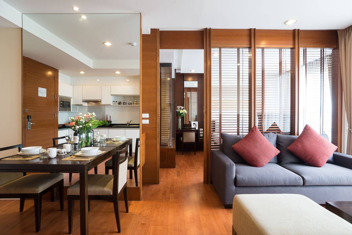 Una sala de estar moderna con un sofá gris, piso de madera y un comedor con mesa para cuatro.
