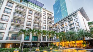 Un hotel con varias plantas, piscina al aire libre y palmeras.