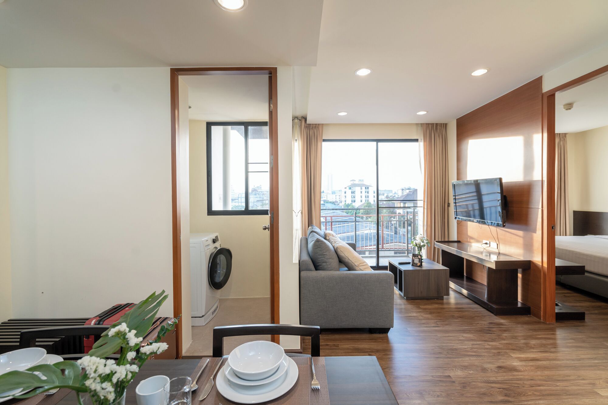 Un apartamento moderno con comedor, sala de estar con sofá, televisor montado en la pared y balcón con vista a la ciudad.