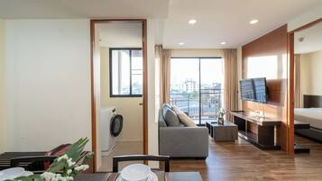 Un apartamento moderno con comedor, sala de estar con sofá, televisor montado en la pared y balcón con vista a la ciudad.