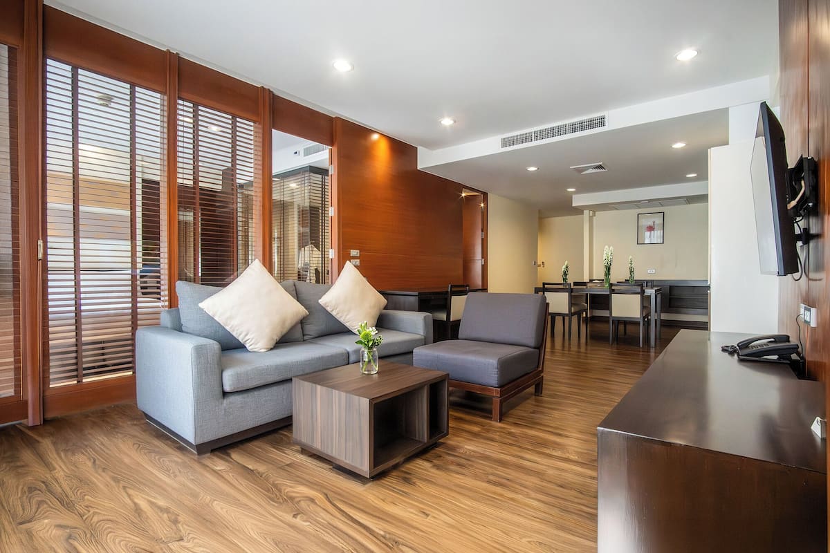 Un moderno vestíbulo de hotel con un conjunto de sofá gris, suelo de madera y un área de comedor con mesa y sillas.