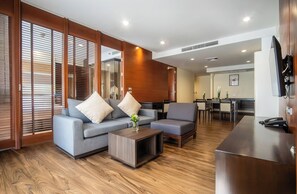 A modern hotel lobby with a grey sofa set, wooden flooring, and a dining area with a table and chairs. - Amanta Hotel & Residence Ratchada (Bangkok)