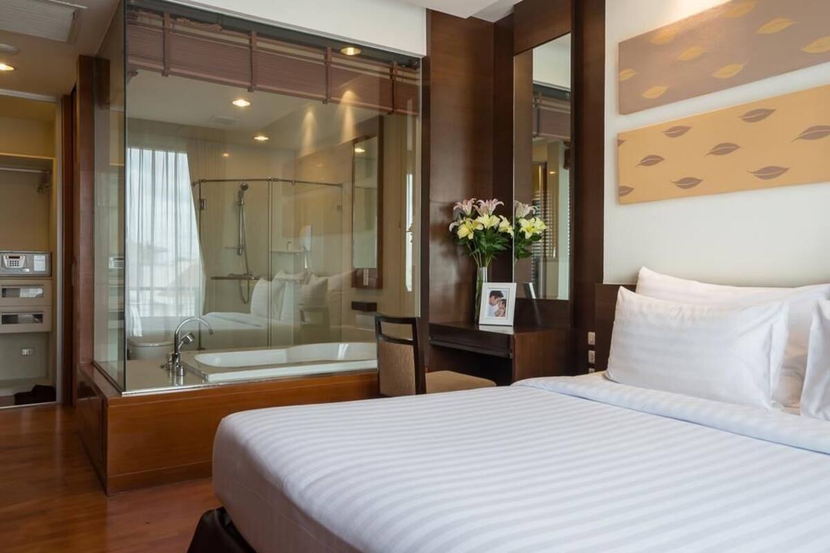 Una habitación de hotel con una cama grande, cabina de ducha con paredes de vidrio, tocador con espejo y un marco de fotos en la cómoda.