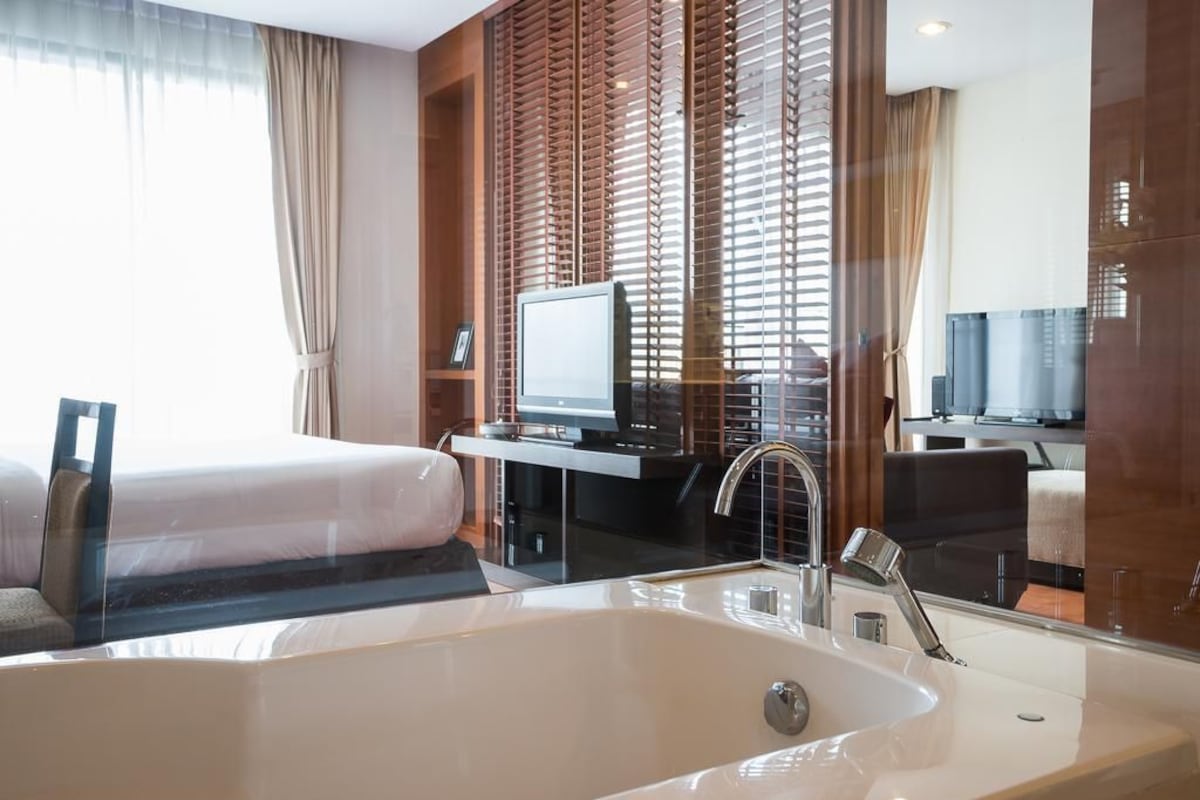 Habitación de hotel con una bañera grande, una cama, un escritorio con televisor y un espejo.