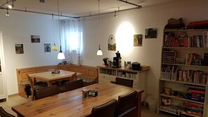 Zona pranzo con tavolo e sedie in legno, una panca integrata, una macchina per il caffè e una libreria piena di libri e giochi.