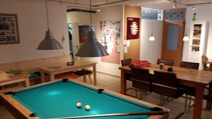 Un tavolo da biliardo con le palle, un'area pranzo con sedie e un tavolo, e una lampada a sospensione.