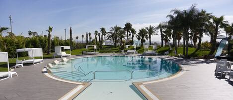 A swimming pool with a curved edge, surrounded by lounge chairs and palm trees.