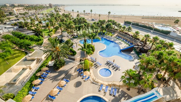 A resort with a large pool, lounge chairs, palm trees, and a beach view. - Gran Palas Hotel - Spa incluido (Vila-Seca)