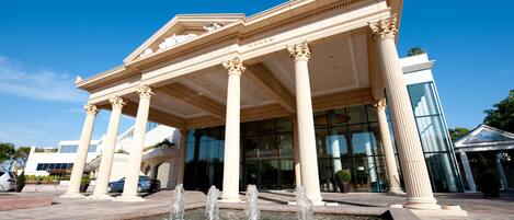 A classical building with columns and a fountain in front.