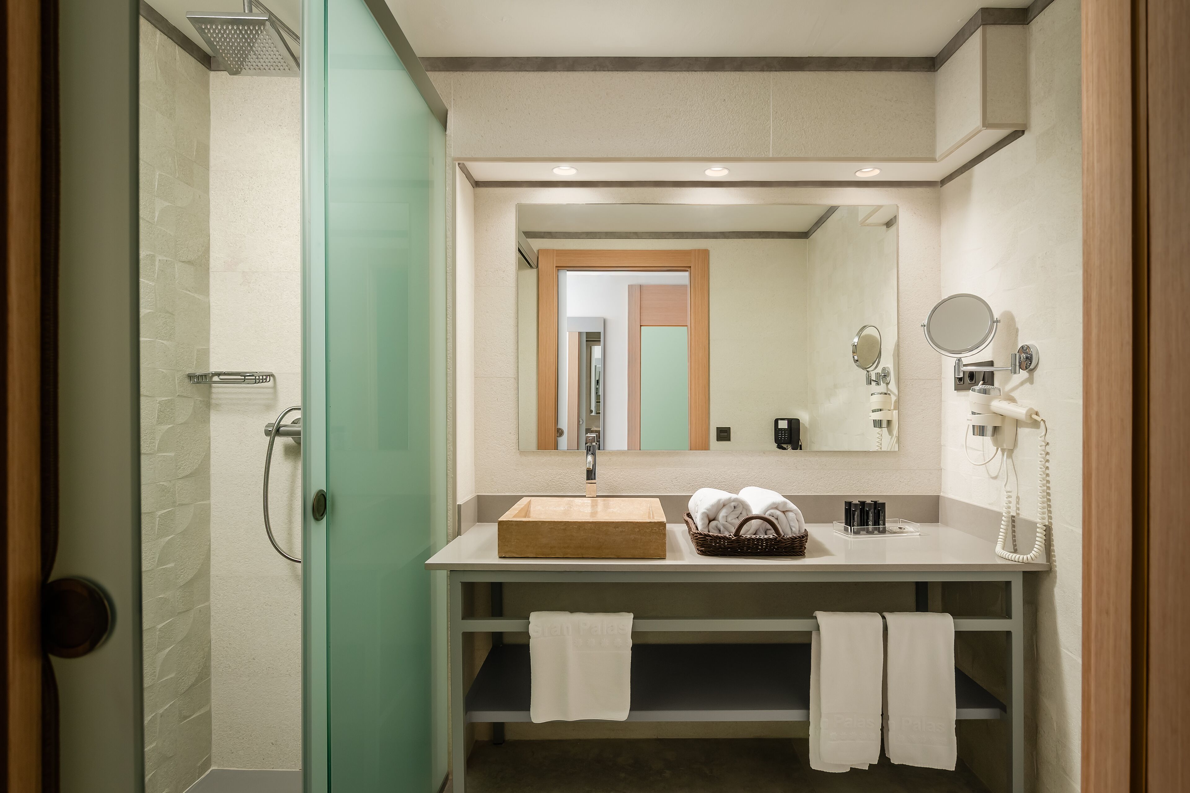 Un baño con ducha, lavamanos y espejo. Hay toallas y artículos de aseo en el mostrador del lavamanos.