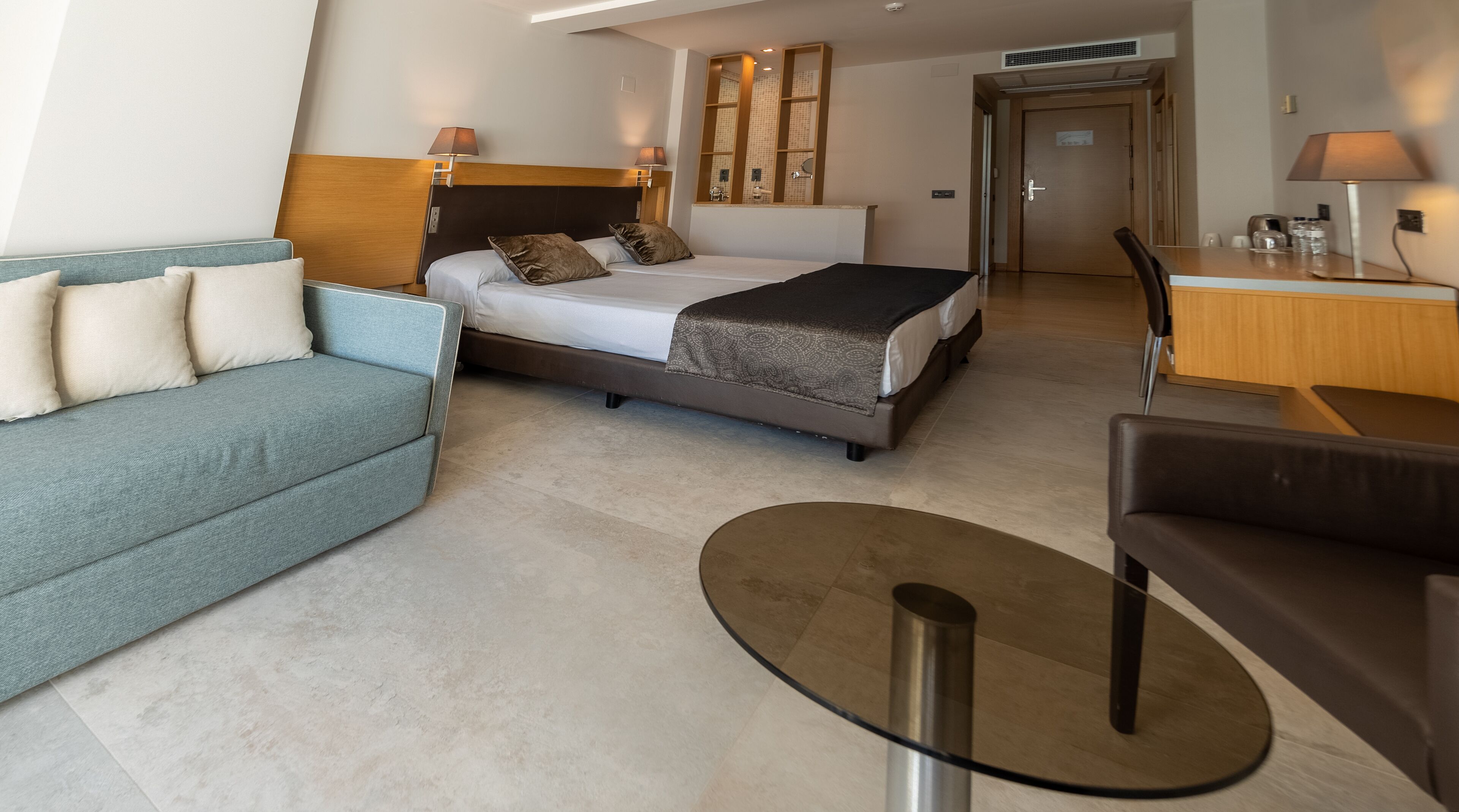 A modern hotel room with a bed, a sofa, a small table, and a desk.