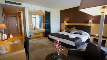 Habitación de hotel con cama, lámparas de noche, escritorio con silla, una mesita con un florero y un espejo.