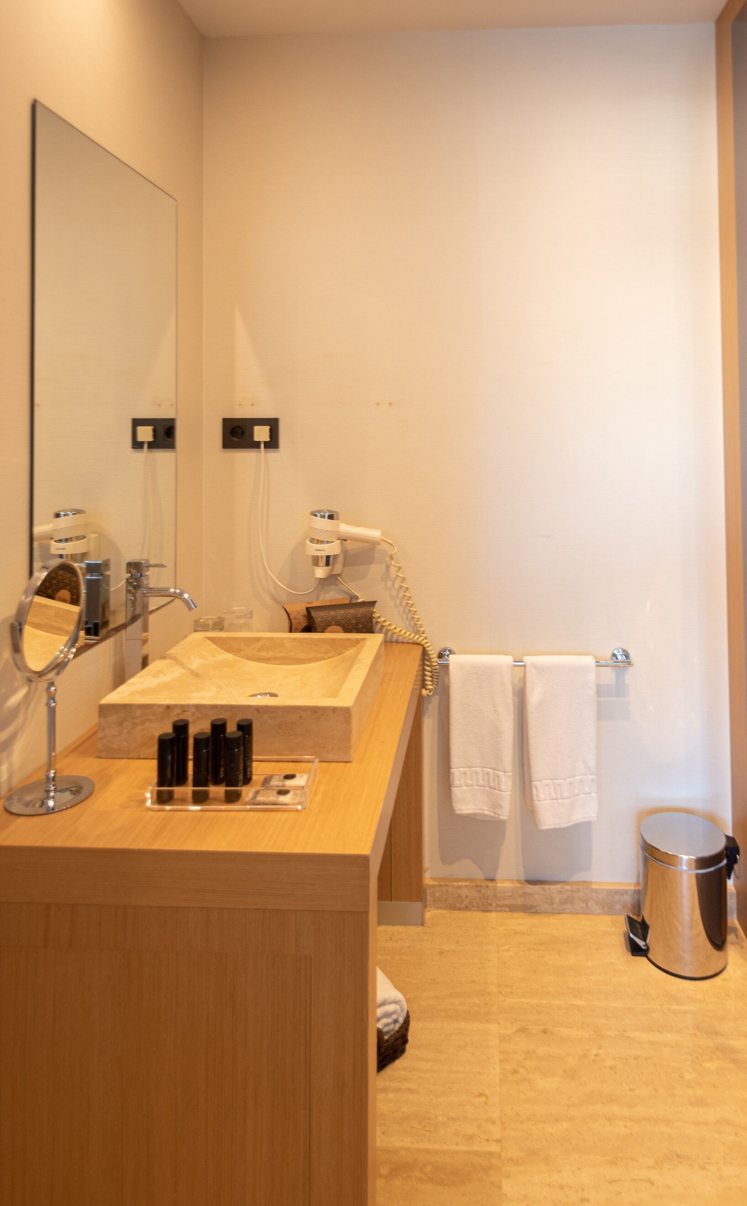Ein modernes Badezimmer mit einem Holzkosmetikschrank, einem Spiegel, einem Föhn und einem Handtuchhalter.