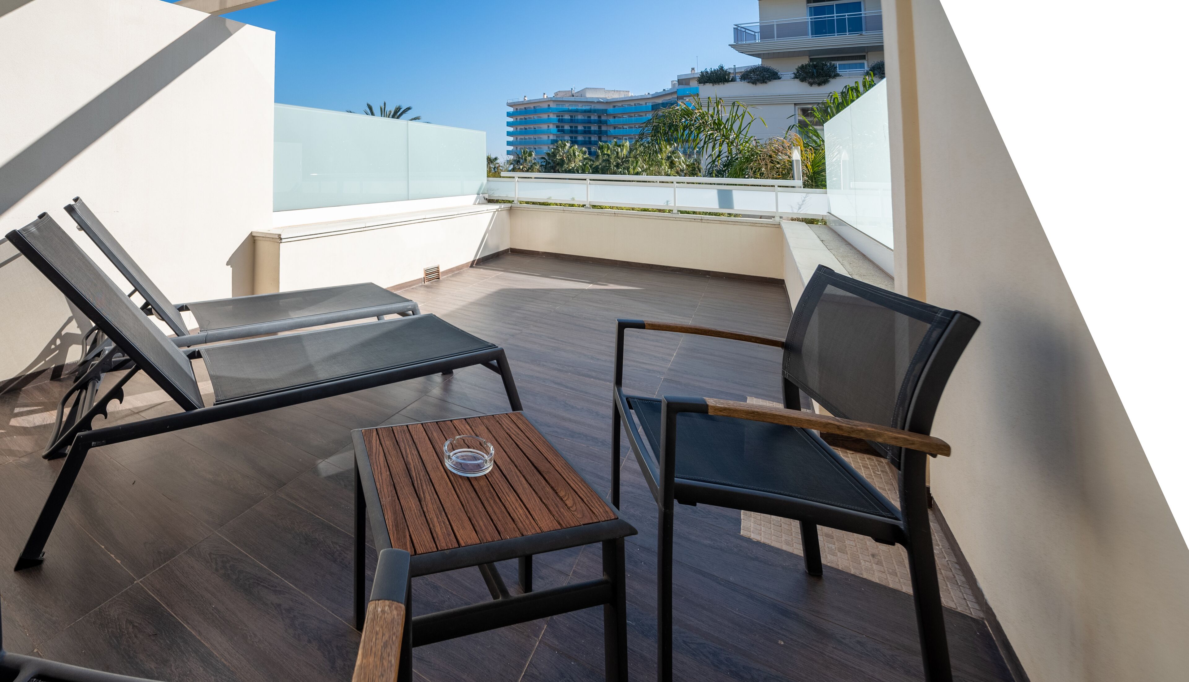 A rooftop terrace with two lounge chairs and a small table, overlooking a cityscape with modern buildings.
