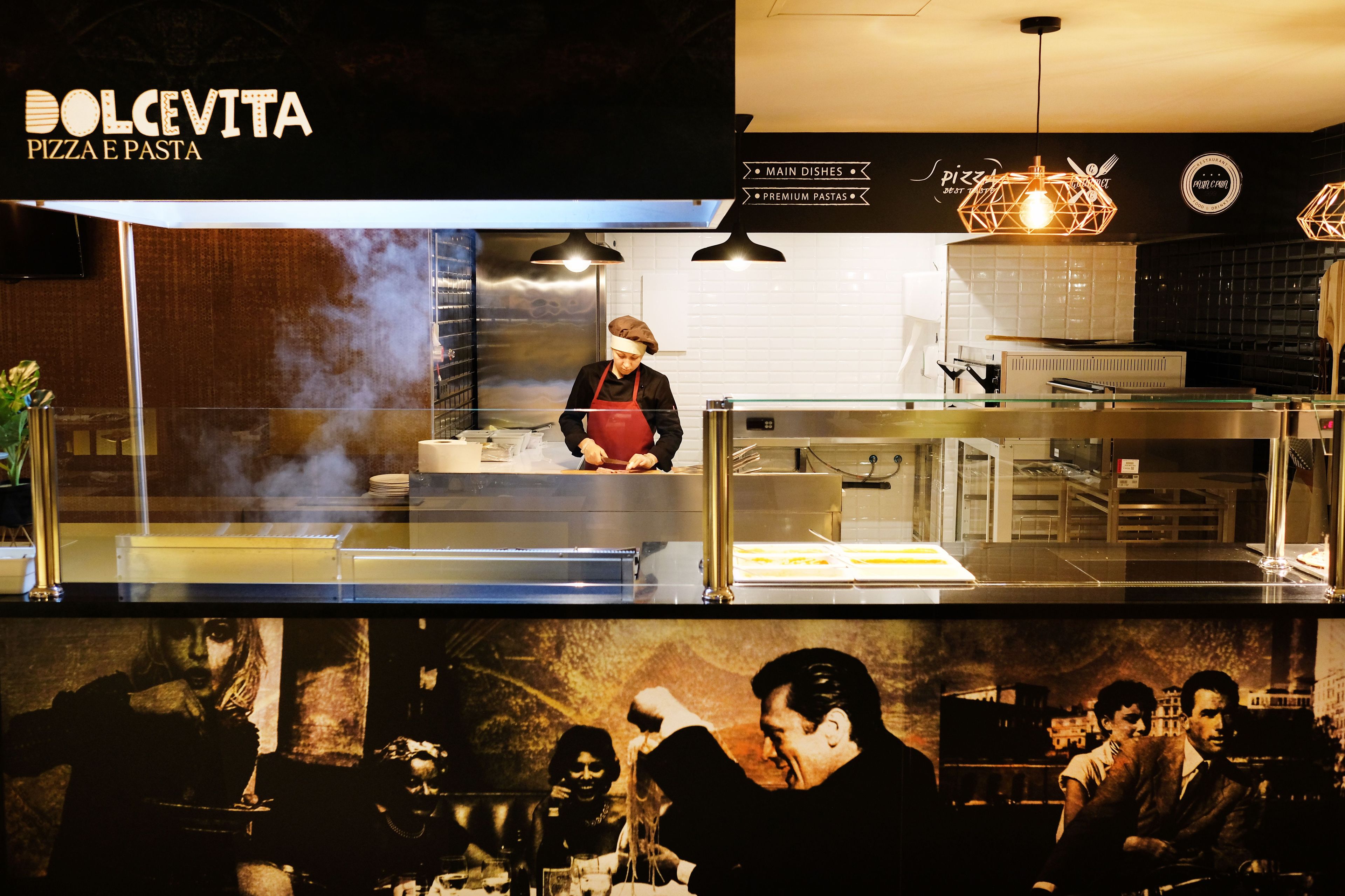 A restaurant interior with a pizza station, a chef at work, and a menu board.