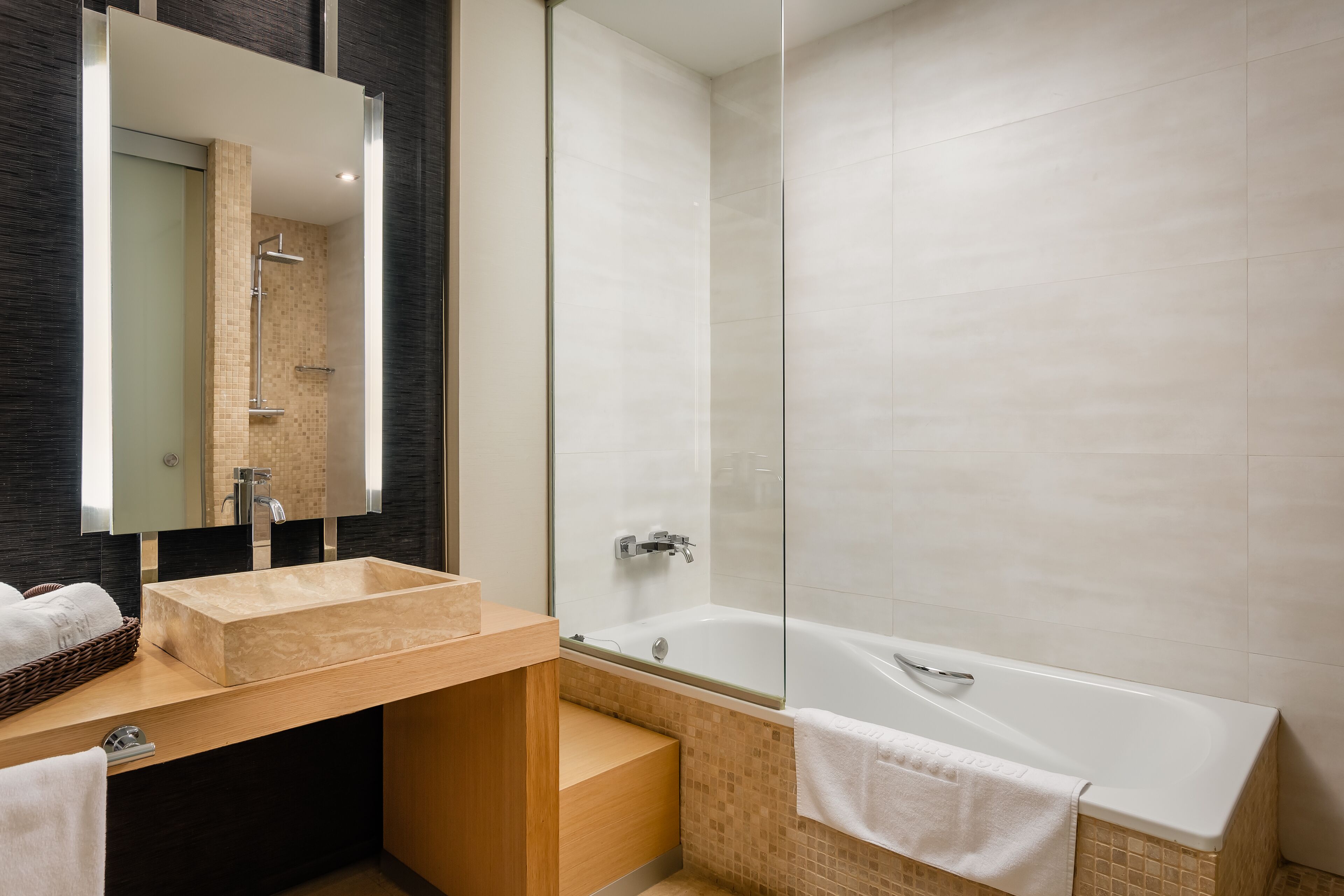 Une salle de bain moderne avec un grand miroir, un meuble-lavabo en bois, un lavabo beige, une douche à parois de verre et une baignoire blanche.