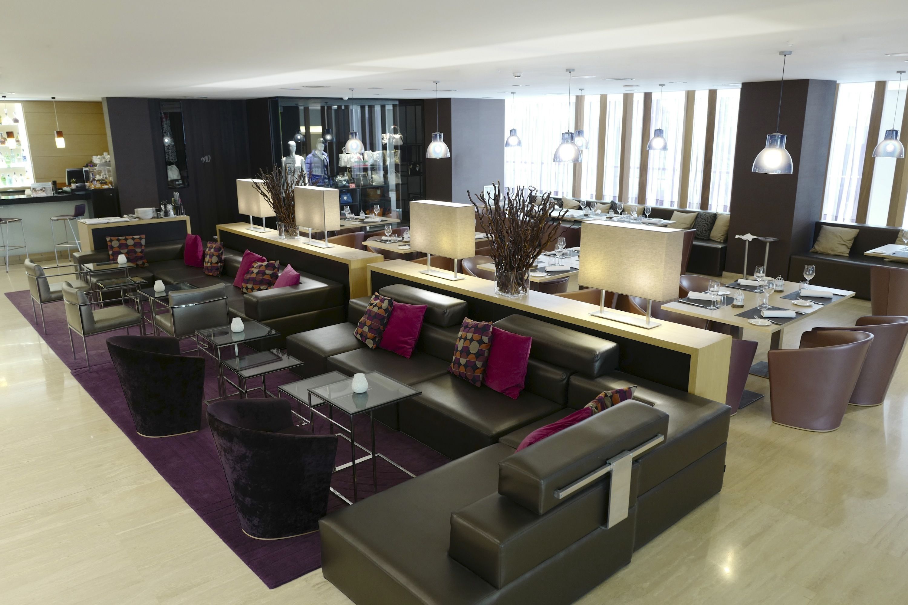 A modern hotel lobby with seating areas, a reception desk, and large windows.