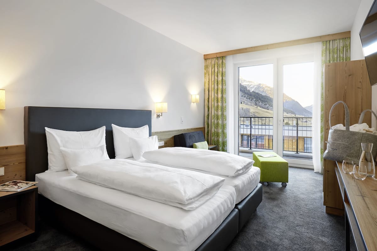 A hotel room with a large bed, a small table with a kettle, and a view of mountains through the window.