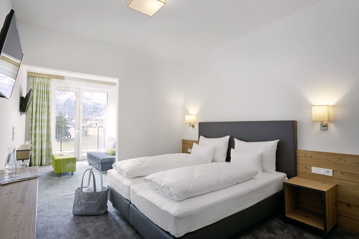 A modern hotel room with a large bed, bedside tables, a desk, and a view of mountains through the window.