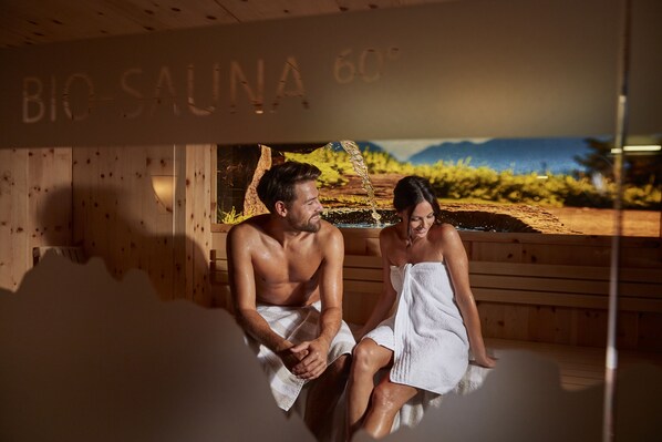 Una pareja en una sauna con paredes de madera y vistas panorámicas.