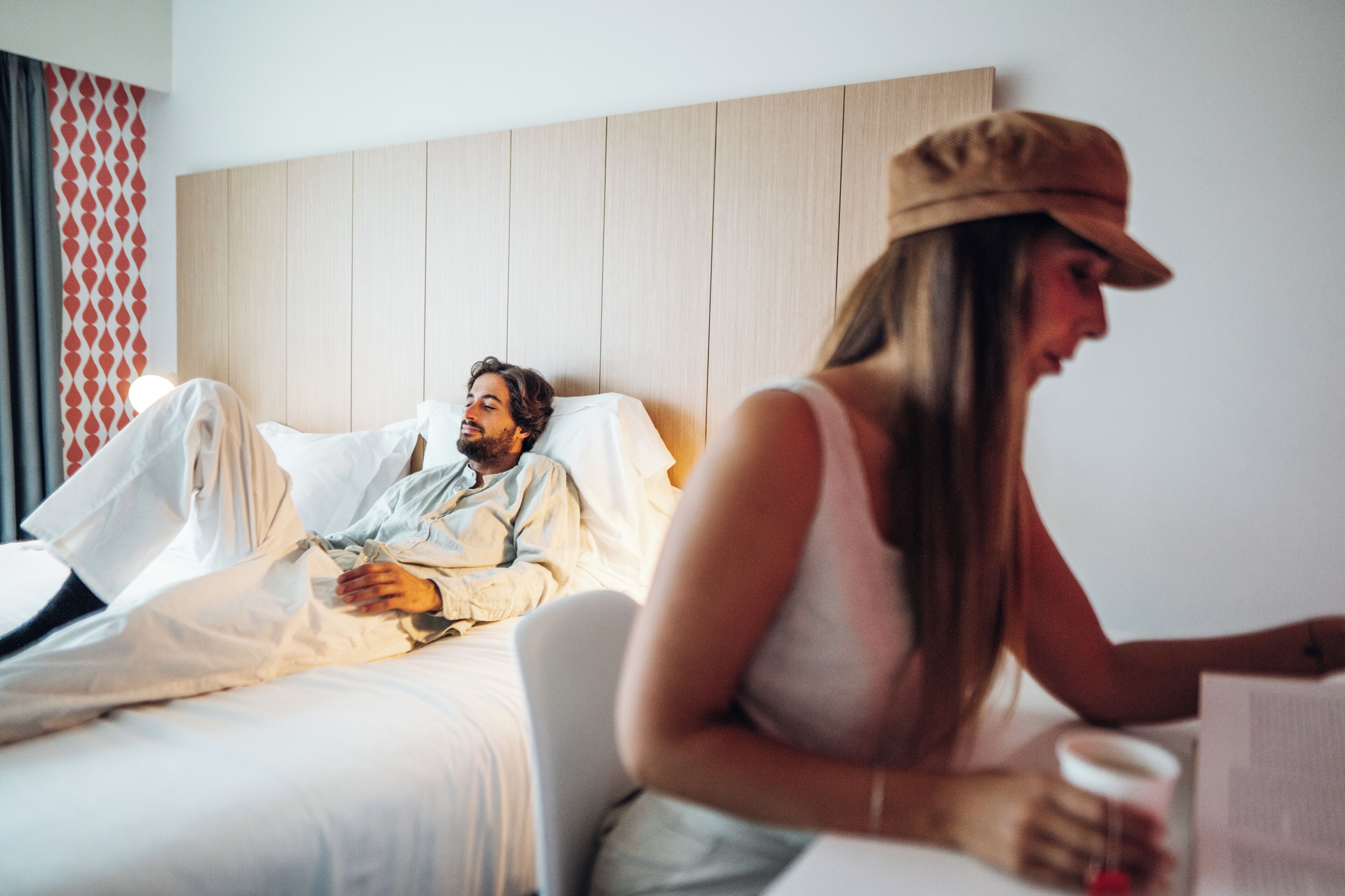 A hotel room with a bed, a bedside table, and a window with curtains.