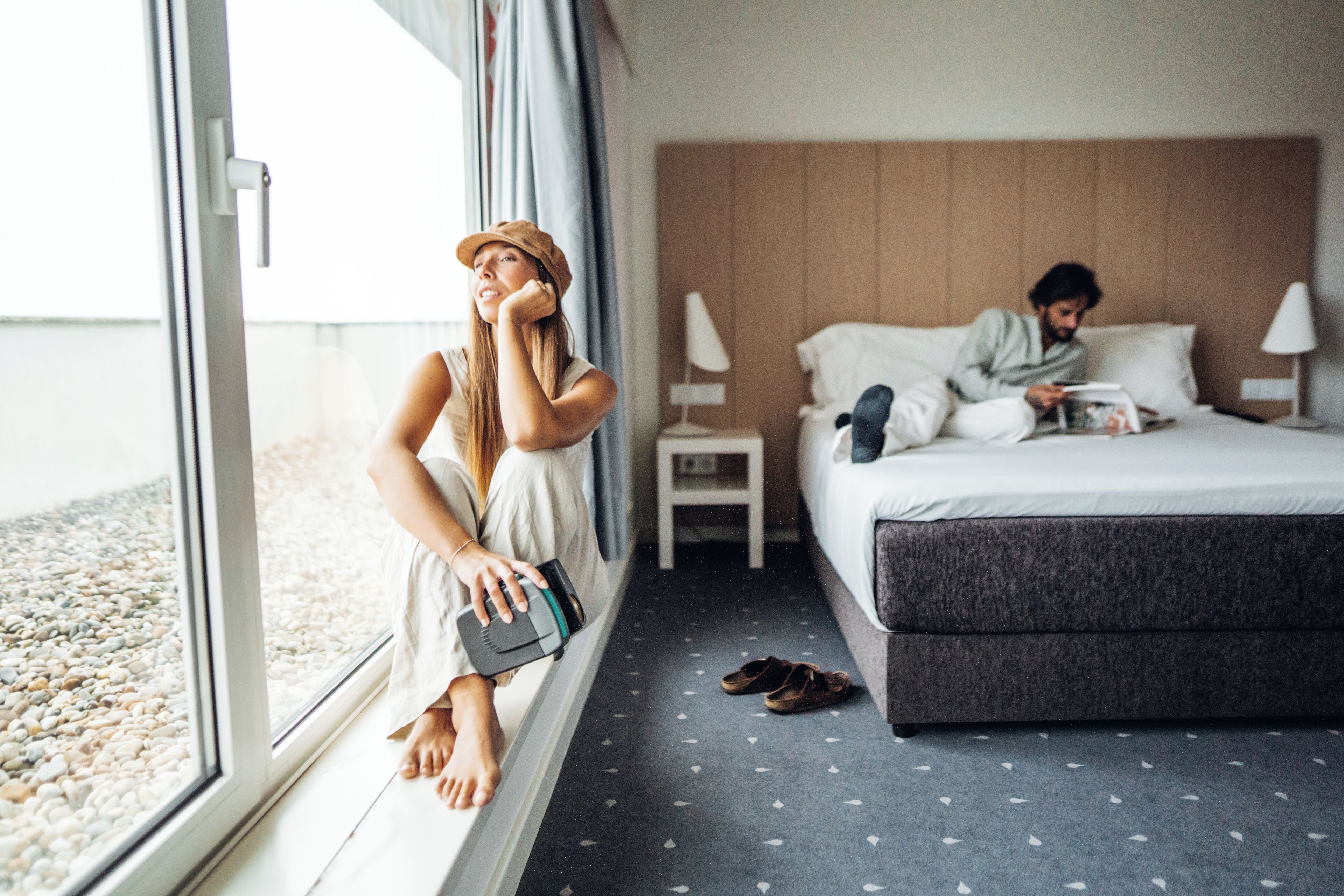 A hotel room with a large window, a bed, a bedside table, and a nightstand.