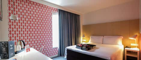 Ein Hotelzimmer mit Bett, Nachttischlampen, einem Schreibtisch mit Fernbedienung, einer Kaffeemaschine und einer Speisekarte.