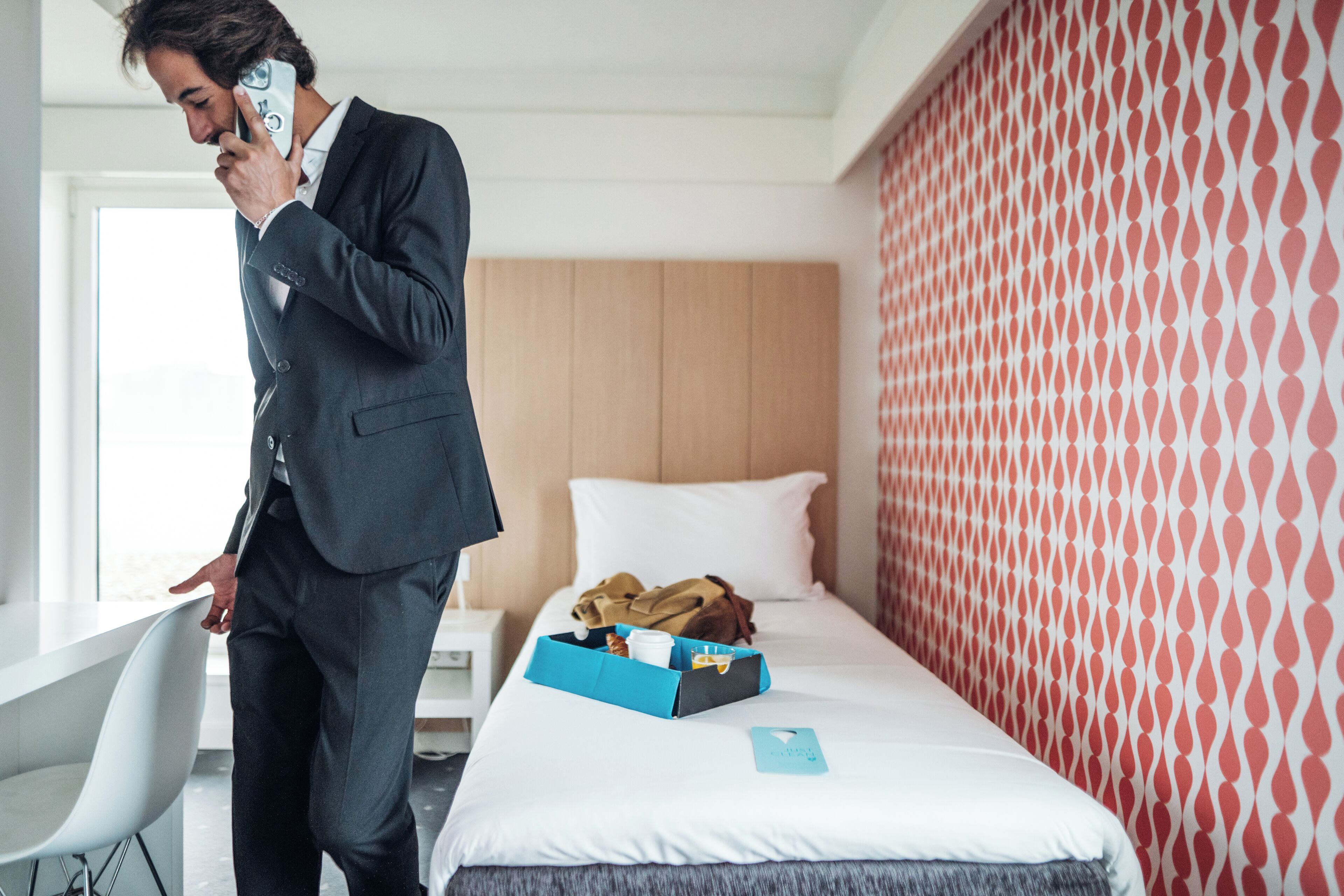 A hotel room with a bed, a bedside table, a chair, and a suitcase on the bed.