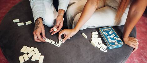 Une personne joue aux dominos sur un pouf rond, avec un jeu de dominos à portée de main.