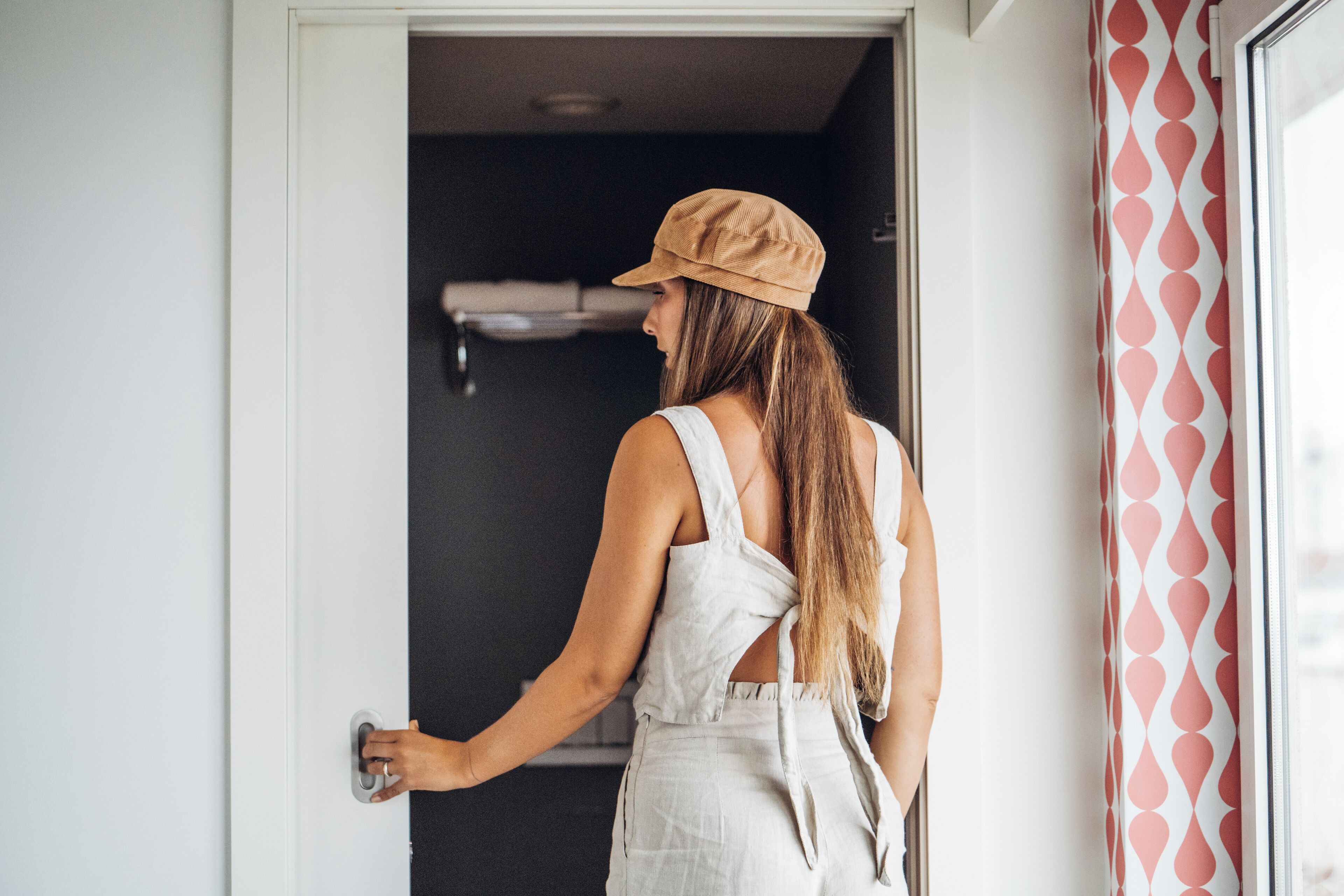 A person opening a door to a room with a black wall and a patterned curtain.