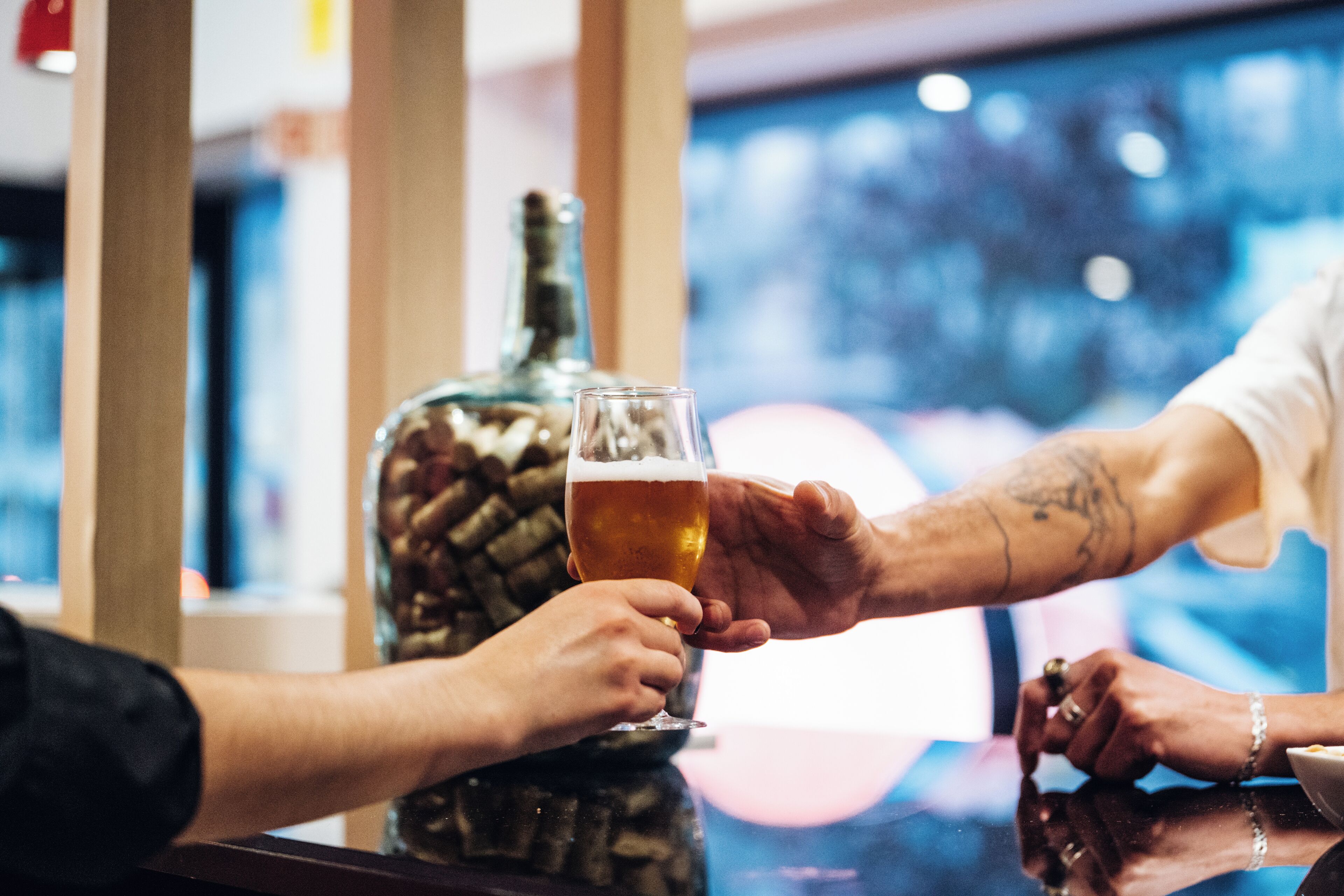 A person holding a glass of beer at a bar with a bottle in the background.