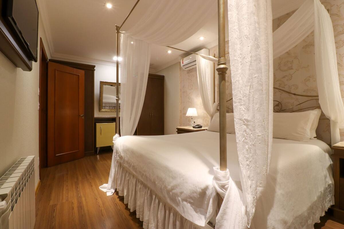 Une chambre à coucher avec un lit à baldaquin, une table de chevet avec une lampe, une porte en bois et un radiateur.