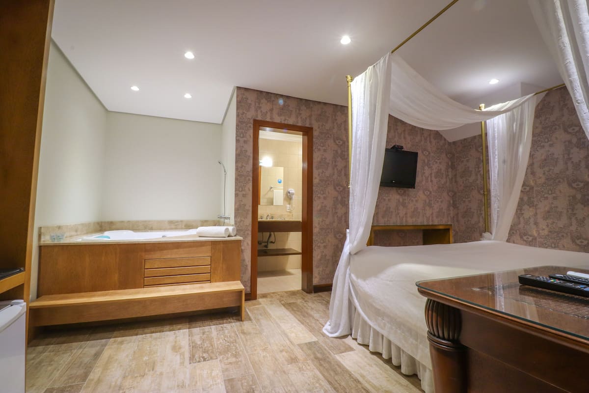 Une chambre à coucher avec un grand lit, un banc en bois, une petite table et un téléviseur fixé au mur.