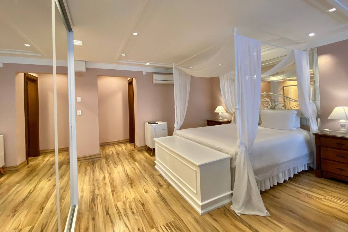 Une chambre à coucher avec un lit à baldaquin, un plancher en bois et une table de chevet blanche.