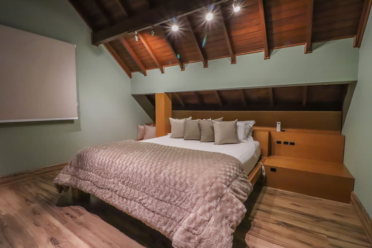 Une chambre avec un plafond en bois, un grand lit recouvert d’une couette rose et une tête de lit agrémentée de plusieurs coussins.