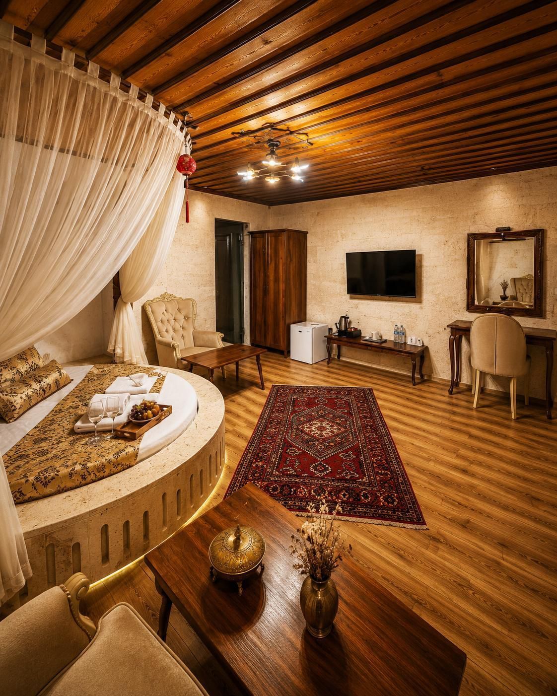 Un dormitorio con una cama, techo de madera, televisor, espejo, mesita pequeña y alfombra roja.