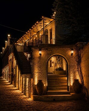 A historic building with a stone facade, arched entrance, and a staircase leading to a balcony. - Saklı Cave House (Avanos)